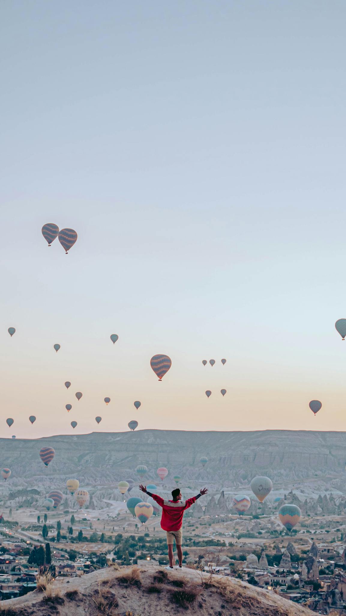A scenic view of hot air balloons soaring over Göreme, Turkey, with a tourist joyfully embracing the panorama.