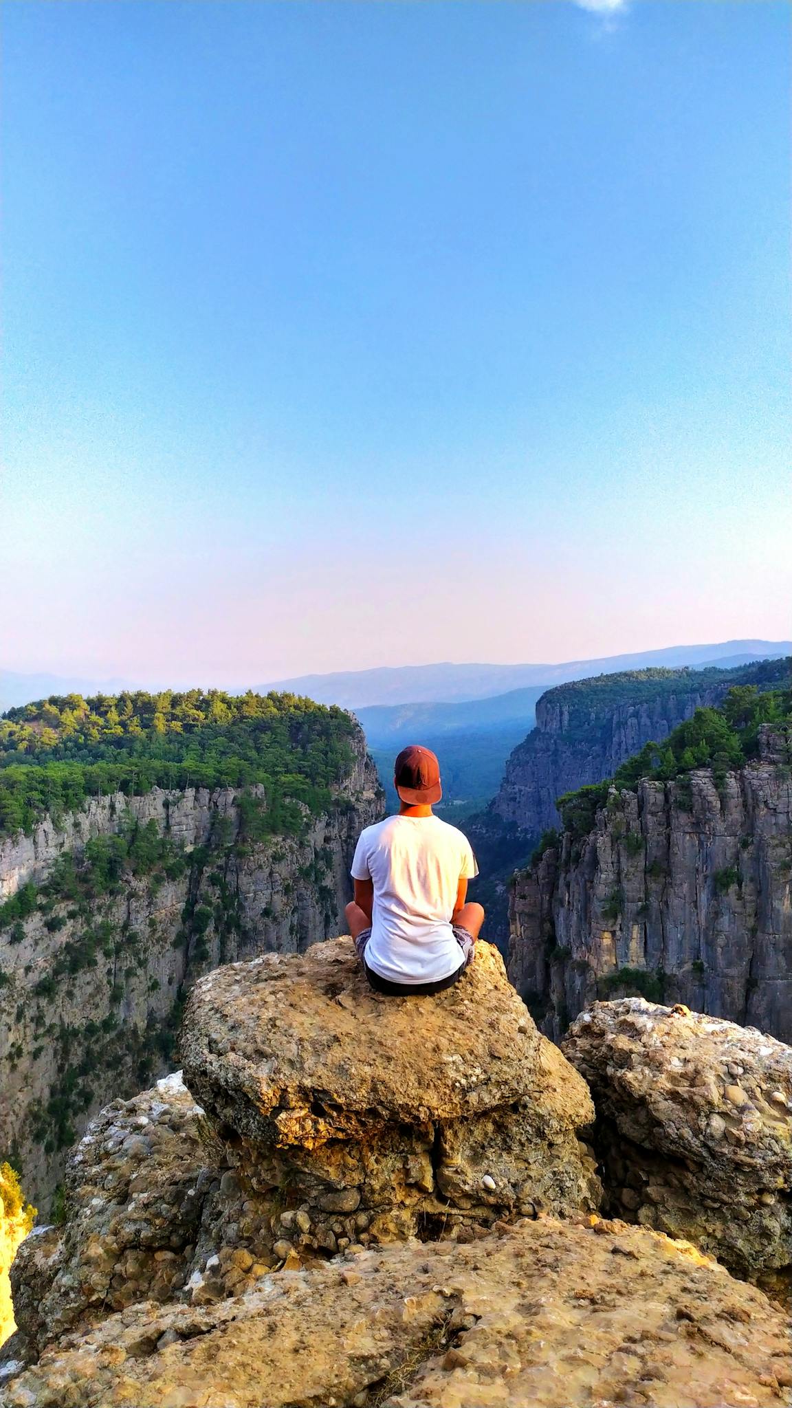 Person sitting on a rocky mountain cliff enjoying breathtaking nature views.