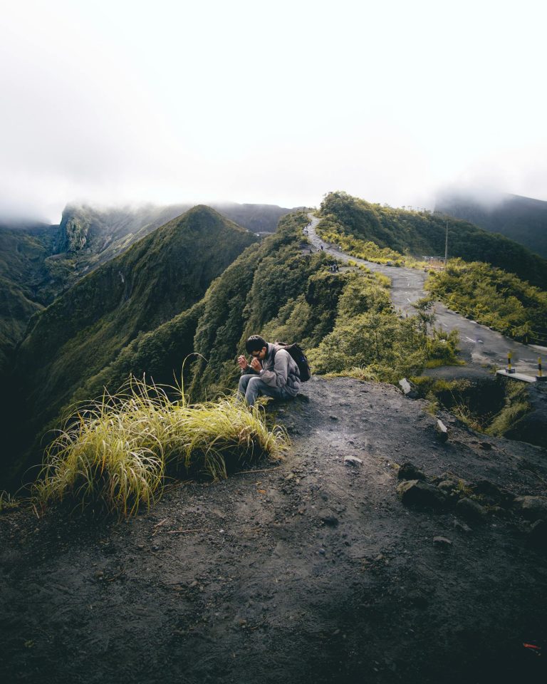 Solo traveler sits on a mountain ridge, capturing breathtaking views under a cloudy sky.