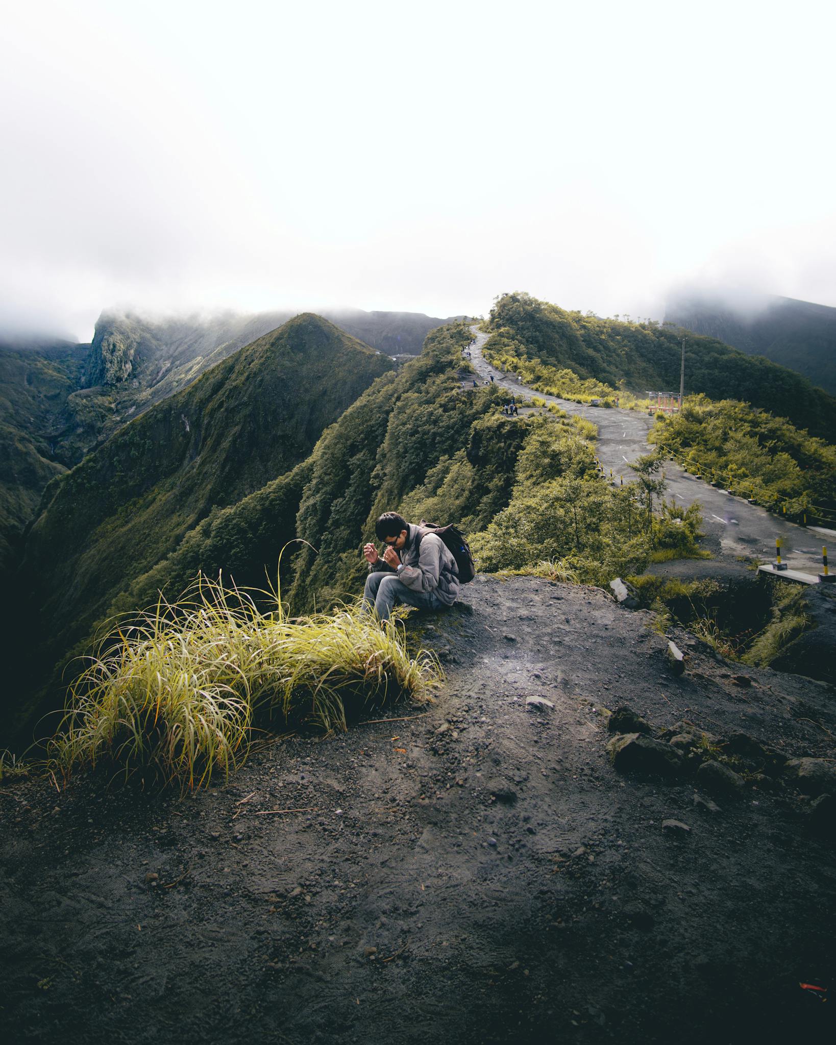 Solo traveler sits on a mountain ridge, capturing breathtaking views under a cloudy sky.