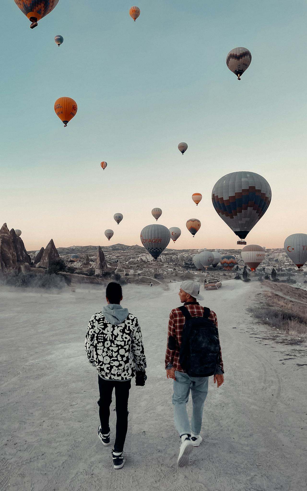 Two people walking in Cappadocia with hot air balloons filling the sky. Perfect for travel enthusiasts.